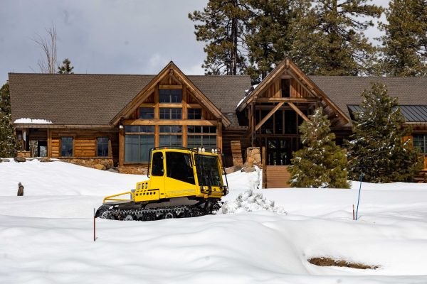 Snowcat pushes snow off the 18th green in front of the golf house.